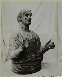 Sculpted bust of a figure with short hair and a draped garment, from Cyprus, one hand raised and one held out