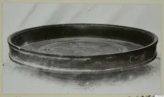 Shallow dark bowl with a spiral scroll motif on its outer wall, photographed on a pale surface