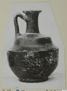 Dark glazed jug with a single loop handle and a flared rim, photographed against a pale backdrop.