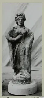 Terracotta figurine of a standing woman with a rolled headdress and draped garment, on a round white base