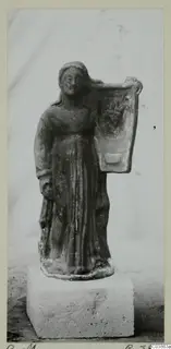 Terracotta figurine of a standing female figure holding a tall flat panel on her shoulder, set on a stone block
