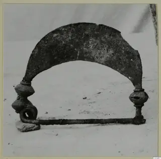 Corroded metal object with an arched plate, two knobbed uprights and a horizontal bar ending in a loop