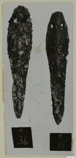 Two corroded metal tools lying side by side on a grey card, with number labels below them.