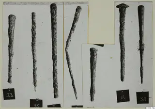Seven corroded bronze tools, long rods tapering to points, shown in separate photographs on a mounted card