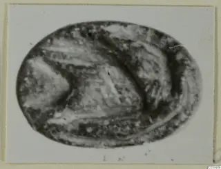 Oval seal or gem of dark stone with an engraved design, photographed close up on a pale card mount.