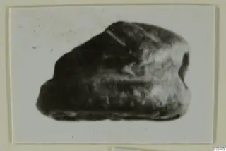 Small dark stone object, identified as a glyptic, in a blurred photograph