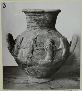 Pottery jar with a flared neck, two handles and raised relief figures on the body, standing on a wooden table