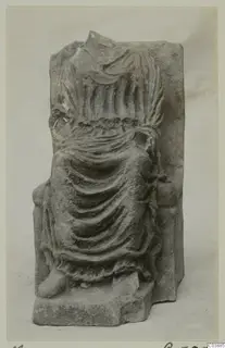 Carved stone fragment of a draped figure with a damaged head, on a rectangular block.