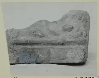 Fragment of a terracotta minor plastic object with a raised ridge and a rounded knob, photographed side-on.
