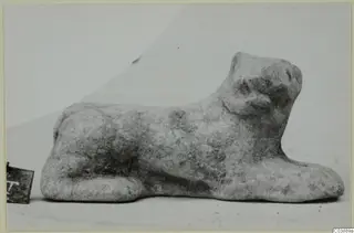 Small terracotta figurine of a crouching animal with its head raised, photographed on a pale background
