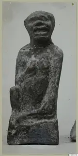 Small seated figure with a rounded head, wide open mouth and a chipped neck, photographed against a pale background.