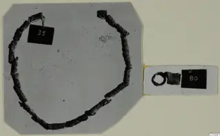 Corroded bronze tubular beads on a loop of wire and a small ring from Lapithos Tomb 322 E, mounted on a card