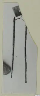 Two long thin metal rods from Lapithos Tomb 322 E, with a small number label at the top