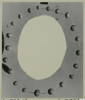 Beads strung on a thin wire in a ring around an oval cut-out on a grey card mount, from Lapithos Tomb 322 E