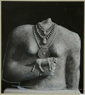Limestone sculpture of a torso with a layered necklace, a disc pendant and a small carved animal on its side