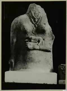 Headless limestone statue torso with a bead necklace, a round pendant and a small animal in relief on the chest