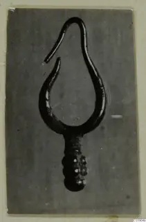 Close-up photograph of a single gold loop-shaped find from Amathus tombs, with a hooked open end and a beaded lower stem