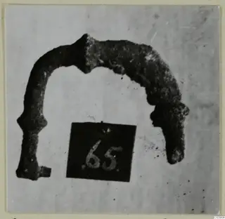 Corroded bronze arched object from Amathus, shown beside a small number label