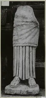 Limestone statue of a standing draped figure, head and arms missing, set on a rectangular base