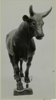 Bronze figure of a bull standing on a small stone base, head turned to one side.