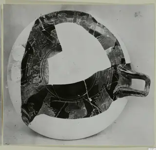Shallow pottery vessel with a single handle, seen from above, partly reconstructed with pale infill