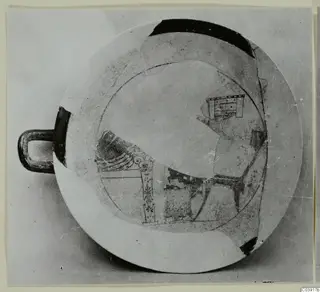 Shallow pottery bowl with a loop handle and dark painted motifs on a pale ground, seen from above
