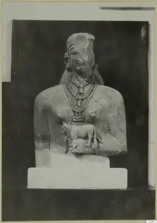 Limestone sculpture of an upper body with layered necklaces and a small animal carved at the chest.