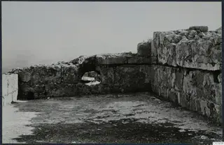 Ruined stone walls and a flat floor surface at Vouni, with a small opening in the lower wall and hazy hills beyond