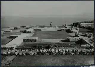 Low stone wall foundations and paved floors at Vouni palace, with a large jar on a base and the sea beyond