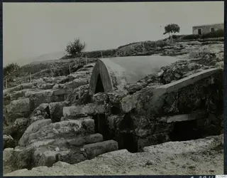 Stone walls and steps at Vouni with a curved white cover over an arched opening, and a stone building beyond.