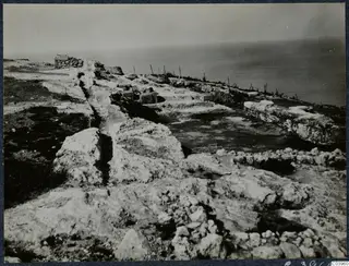 Ruined stone walls and scattered stone blocks on a rocky coastal headland at Vouni, with the sea beyond
