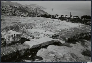 Stone foundations of the Temple of Athena at Vouni, with a fenced hillside and the sea beyond.