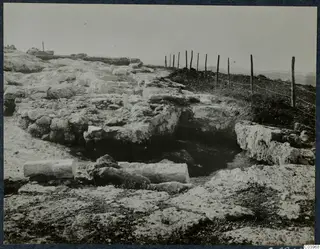 Ruined stone remains at Vouni Temple of Athena, with a wire fence along a hilltop and distant hills