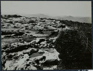 Pale rock ground at Vouni with cut channels and shallow pools, a wire fence on the right and hills behind