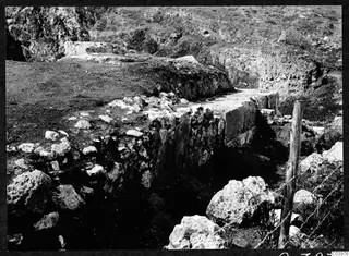Excavated stone wall at the Soli theatre, with loose stones and a wooden fence post with barbed wire