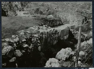Excavated stone wall at the theatre of Soli, with loose stones and a wooden fence post at the right.