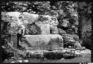 Large cut stone blocks in a stepped arrangement against a rubble wall at the theatre at Soli, with small plants growing at the base.