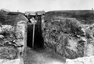 Narrow stone-walled passage at Soli, its top spanned by two large stone slabs propped on a timber beam and upright post.