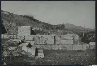 Ashlar stone wall and steps of the theatre at Soli, with a hillside and wire fence behind.