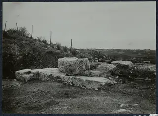 Large cut stone blocks forming a step-like structure on a slope at the theatre at Soli, with a wire fence behind.