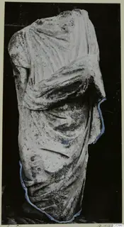 Marble statue fragment of a draped figure, headless, with one arm bent across the body.