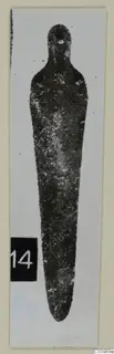 Bronze tool with a loop at one end and a long tapering blade, from Lapithos, shown upright on a white card