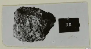 Corroded lump of metal with a rough, pitted crust, beside a small number label