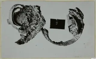 Corroded bronze fragments of personal adornments, with a black number card, from the Vrysi tou Barba tombs at Lapithos