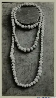 Three strands of pale, speckled beads of graduated sizes laid out on grey cloth