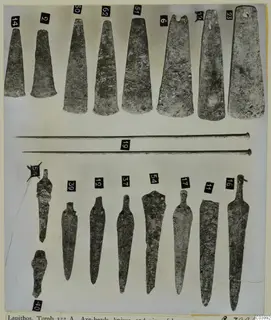 Bronze axe-heads, knives, daggers and pins from Lapithos Tomb 322A, laid out in rows with numbered labels.