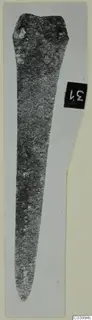 Long tapering metal blade with two small holes at its broad end, shown upright on a pale card
