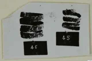 Two groups of dark, corroded metal objects on a white card, each beside a black number label.