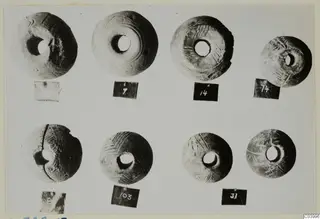 Eight disc-shaped objects with central holes and incised patterns, in two rows, small finds from L.322E.