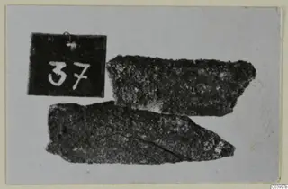 Two corroded metal fragments beside a number label, from Lapithos Tomb 322 D